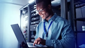 MAN IN A DATA CENTER WORKING ON A LAPTOP